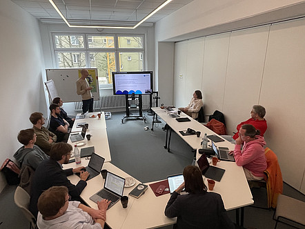 [Translate to Englisch:] Gruppe von Workshop-Teilnehmenden schaut Mann bei Präsentation zu.